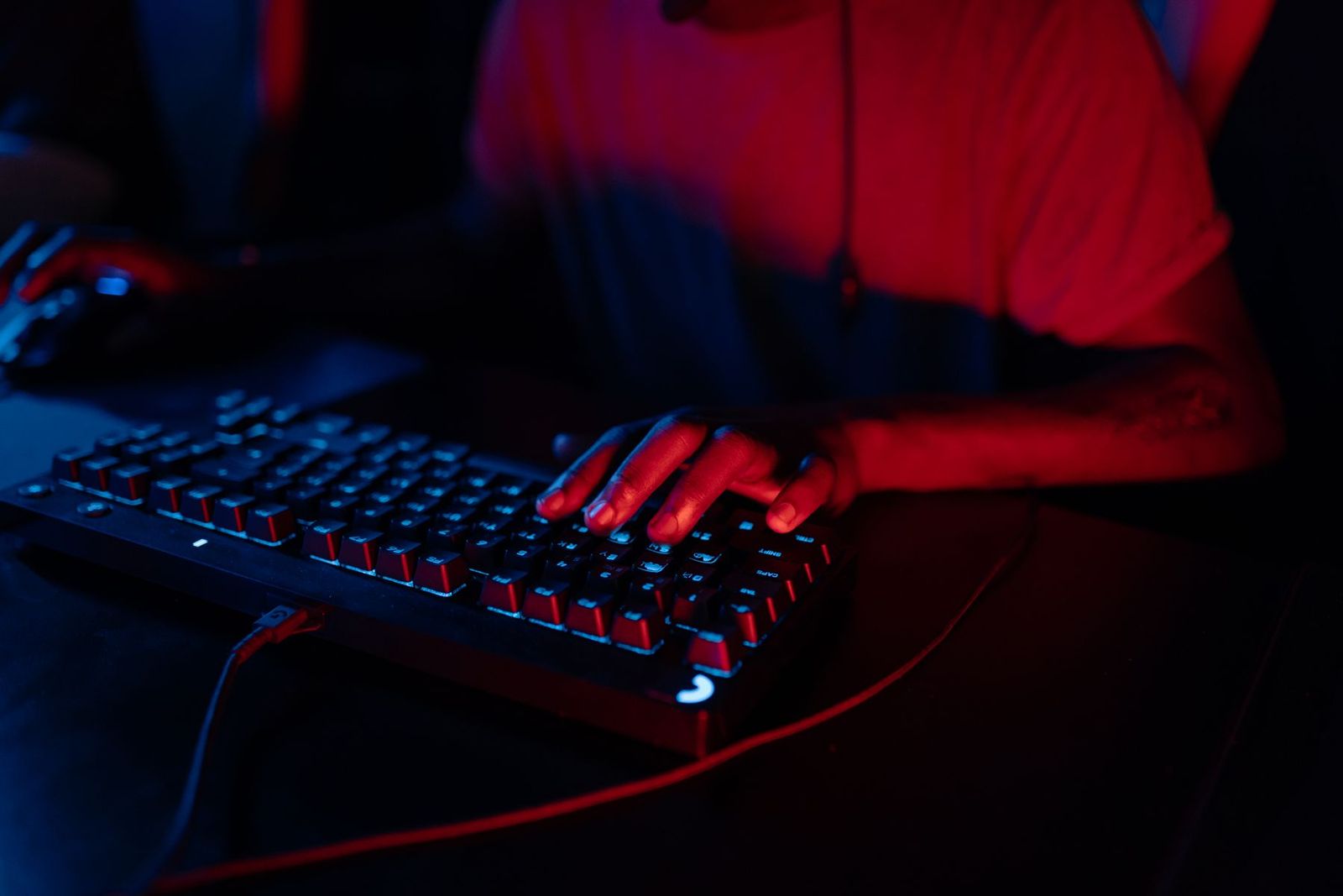 붉고 푸른 빛 아래 RGB 키보드를 치는 손